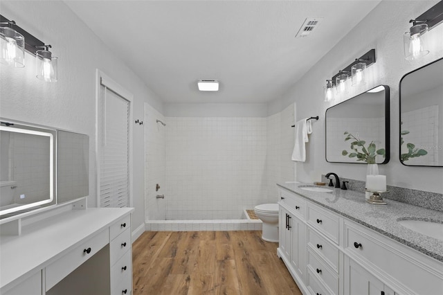 bathroom featuring hardwood / wood-style floors, vanity, toilet, and a tile shower