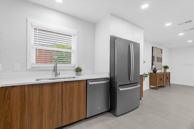 kitchen with white cabinets, sink, stainless steel appliances, and light hardwood / wood-style flooring