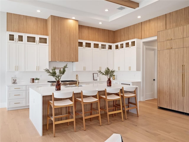 kitchen with light hardwood / wood-style floors, an island with sink, a breakfast bar area, white cabinets, and sink