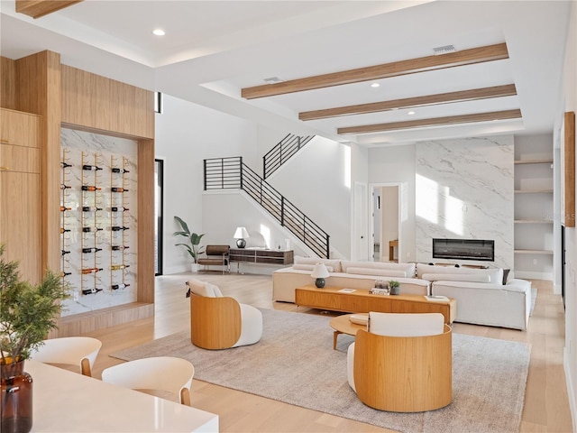 living room with a fireplace, built in shelves, beamed ceiling, and light wood-type flooring