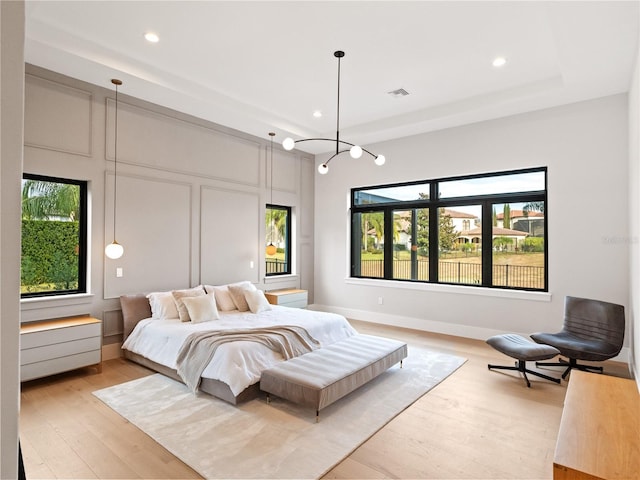 bedroom with a raised ceiling and light wood-type flooring