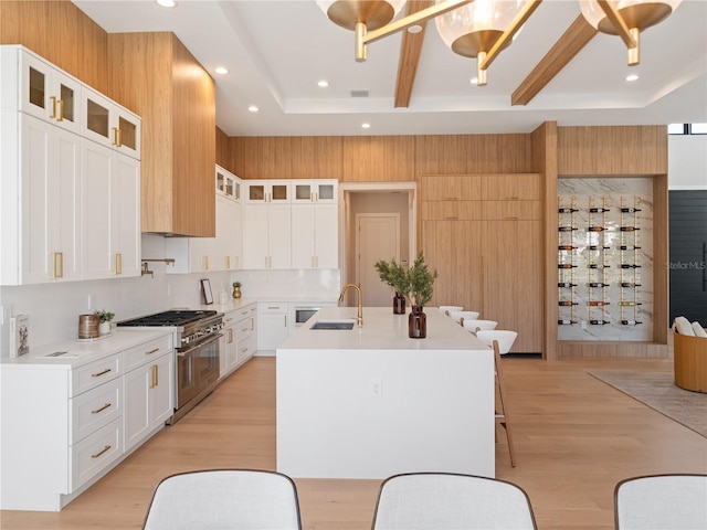 kitchen featuring an island with sink, range with two ovens, white cabinets, light hardwood / wood-style flooring, and sink