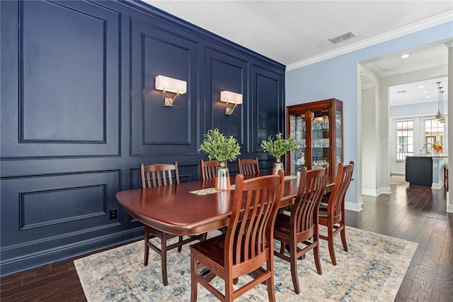 dining area featuring sink, dark hardwood / wood-style flooring, a textured ceiling, and ornamental molding