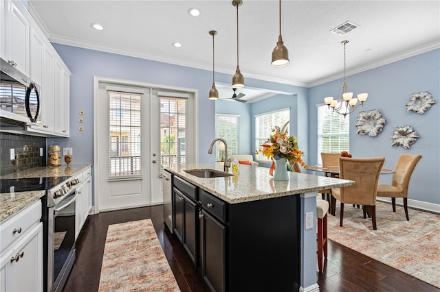 kitchen with white cabinetry, stainless steel appliances, hanging light fixtures, and an island with sink