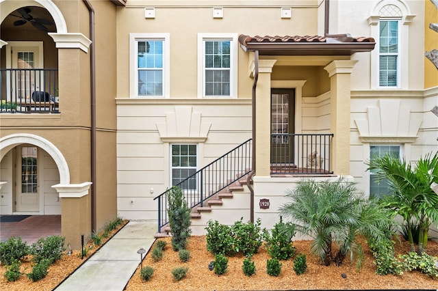 view of exterior entry featuring ceiling fan, a tiled roof, and stucco siding