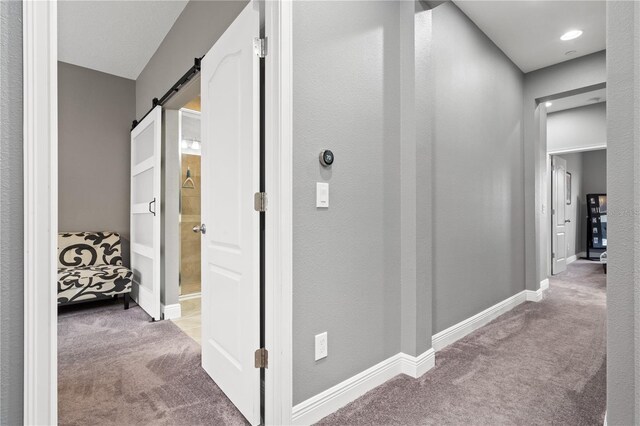 corridor with carpet floors, a barn door, and baseboards