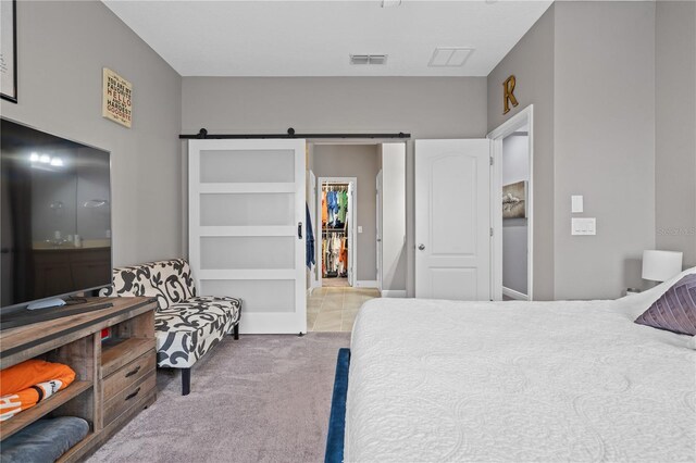 bedroom with a barn door, visible vents, a closet, carpet, and a walk in closet