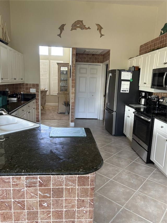 kitchen featuring backsplash, white cabinets, light tile patterned floors, kitchen peninsula, and stainless steel appliances