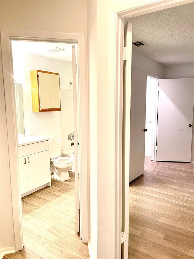 corridor with a textured ceiling and light hardwood / wood-style flooring