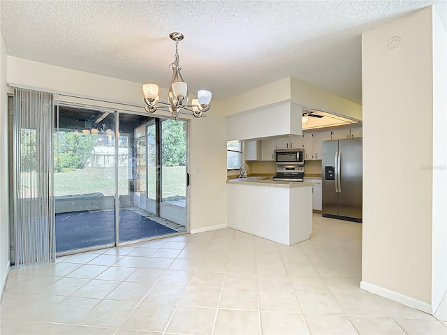 kitchen with stainless steel appliances, an inviting chandelier, kitchen peninsula, a textured ceiling, and light tile patterned floors