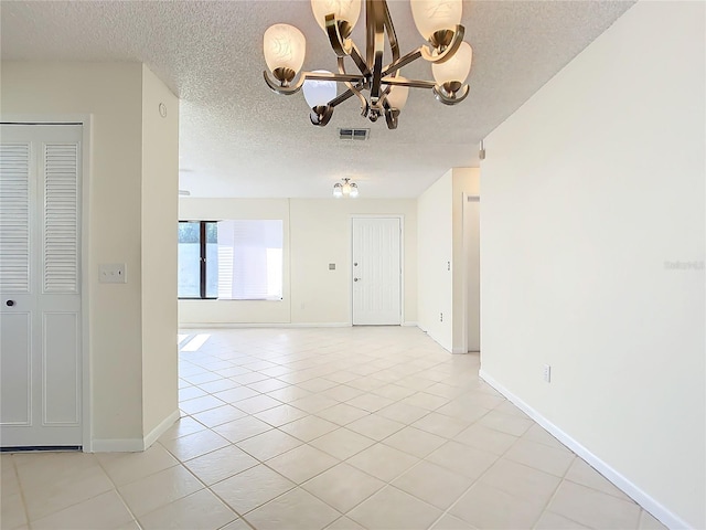 empty room with a notable chandelier, light tile patterned floors, and a textured ceiling