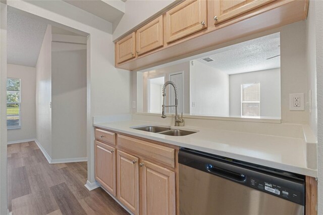 kitchen with light brown cabinets, sink, stainless steel dishwasher, a textured ceiling, and light wood-type flooring