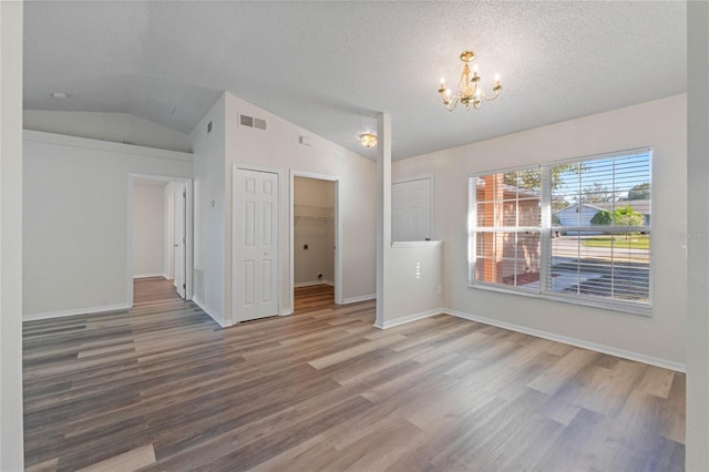 unfurnished room with hardwood / wood-style floors, a textured ceiling, lofted ceiling, and a notable chandelier