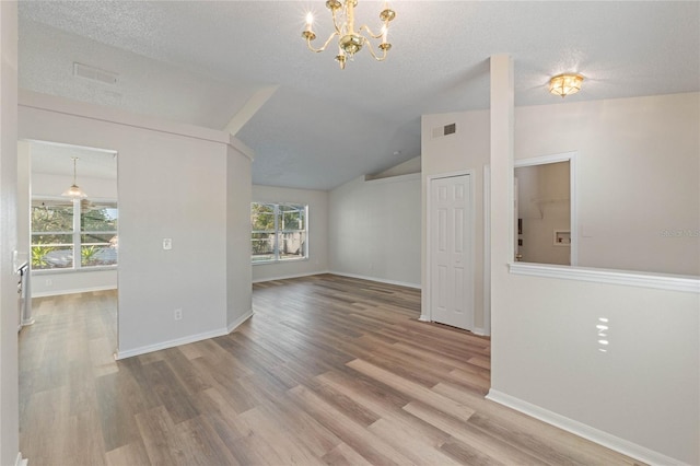 unfurnished living room with a textured ceiling, hardwood / wood-style floors, lofted ceiling, and a notable chandelier