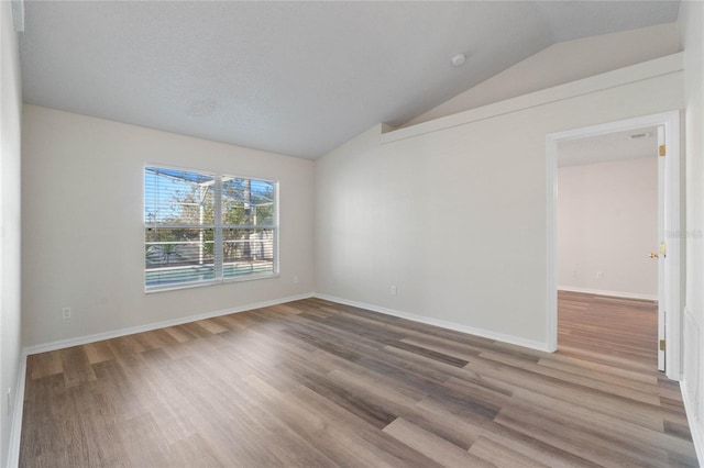 spare room featuring a textured ceiling, hardwood / wood-style flooring, and vaulted ceiling