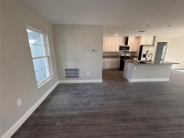 kitchen with dark wood-type flooring, white cabinetry, stainless steel appliances, an island with sink, and dark stone counters