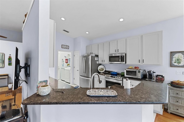 kitchen featuring white cabinets, independent washer and dryer, light hardwood / wood-style floors, kitchen peninsula, and stainless steel appliances