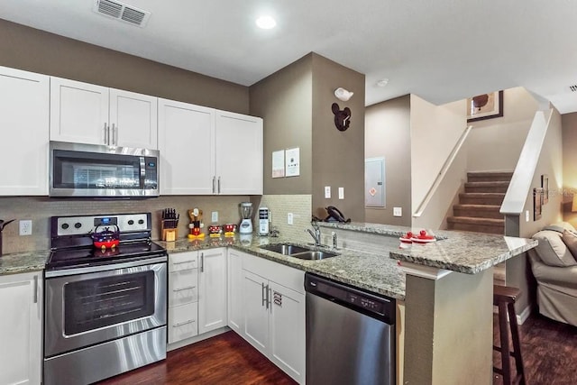 kitchen featuring kitchen peninsula, a kitchen bar, backsplash, stainless steel appliances, and white cabinetry