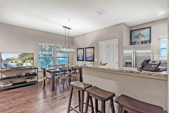 kitchen with dark hardwood / wood-style floors, stainless steel fridge, light stone countertops, and hanging light fixtures