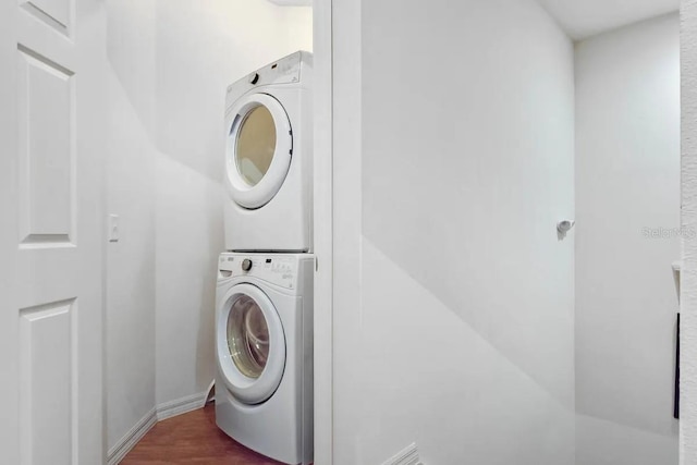 laundry room with dark wood-type flooring and stacked washer / drying machine