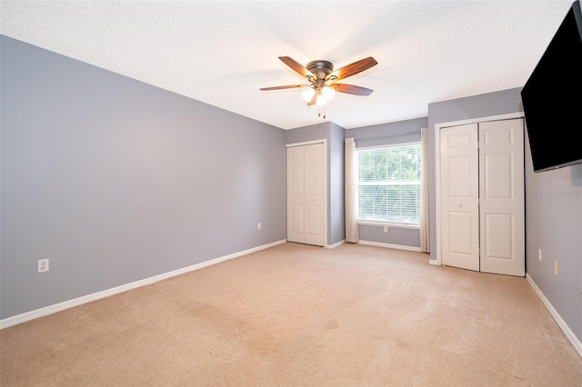 unfurnished bedroom with light carpet, a textured ceiling, ceiling fan, and multiple closets