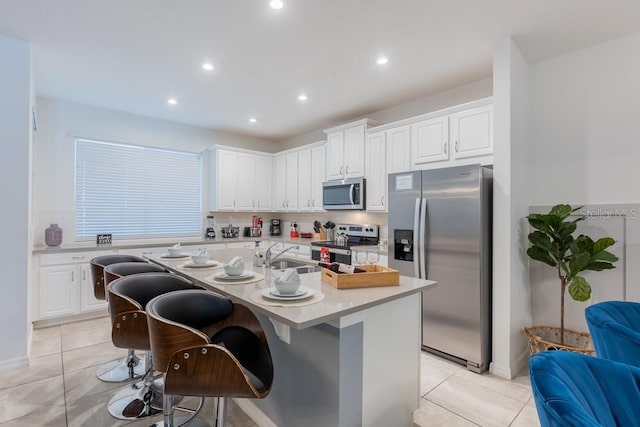 kitchen featuring appliances with stainless steel finishes, a center island with sink, white cabinetry, and a kitchen breakfast bar