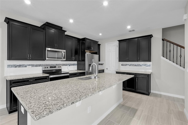 kitchen featuring a center island with sink, light stone countertops, appliances with stainless steel finishes, and tasteful backsplash