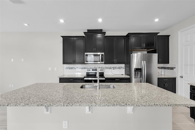 kitchen featuring sink, a kitchen island with sink, decorative backsplash, a breakfast bar, and appliances with stainless steel finishes