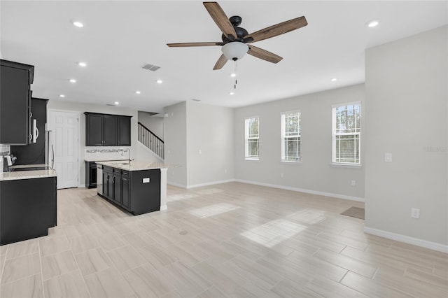 kitchen featuring a center island with sink, light stone counters, ceiling fan, and sink