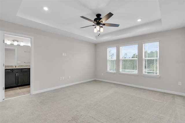 carpeted empty room featuring a raised ceiling, ceiling fan, and a healthy amount of sunlight