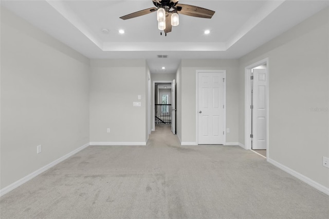 interior space with a raised ceiling, light carpet, and ceiling fan