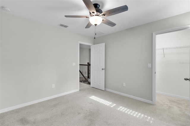 unfurnished bedroom with a closet, a walk in closet, light colored carpet, and ceiling fan