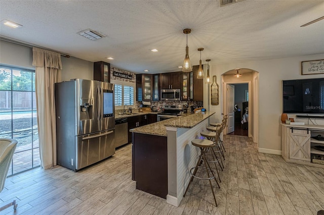 kitchen featuring dark brown cabinetry, light hardwood / wood-style floors, decorative light fixtures, and appliances with stainless steel finishes