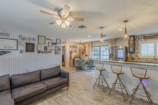 living room with ceiling fan, sink, a textured ceiling, and light wood-type flooring