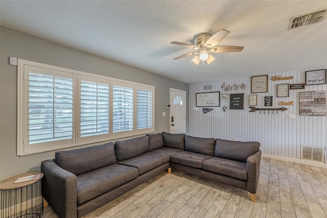 living room featuring visible vents, a textured ceiling, wallpapered walls, and ceiling fan