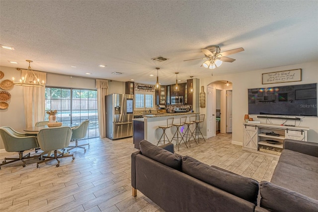 living room featuring ceiling fan with notable chandelier, light wood-type flooring, and a textured ceiling