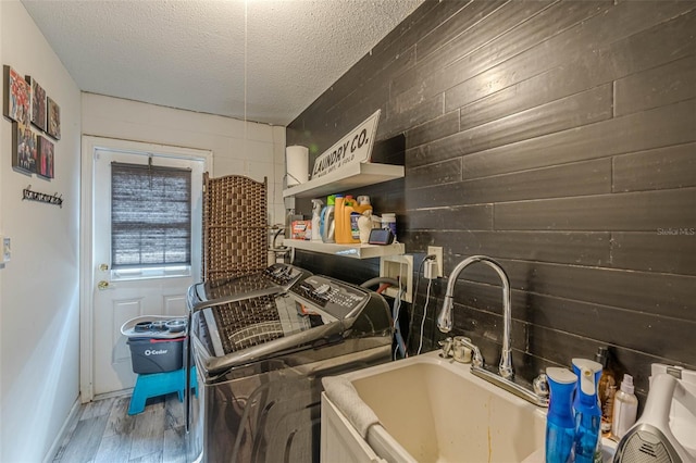 laundry area featuring wood walls, sink, a textured ceiling, wood-type flooring, and washing machine and clothes dryer