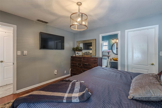 bedroom featuring visible vents, a textured ceiling, baseboards, and wood finished floors