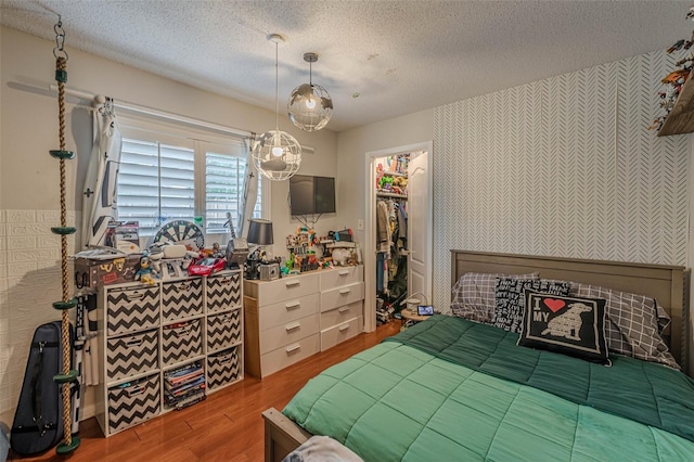 bedroom with a spacious closet, wood-type flooring, and a textured ceiling