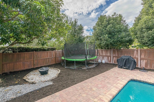 view of patio / terrace with a trampoline, a fenced in pool, and a grill