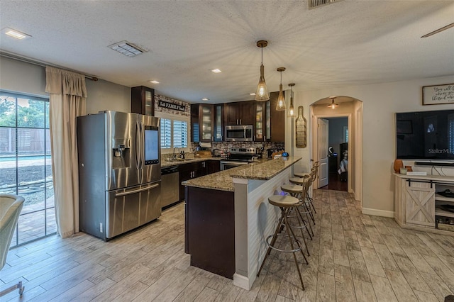 kitchen with glass insert cabinets, light wood-style flooring, a kitchen breakfast bar, appliances with stainless steel finishes, and a peninsula