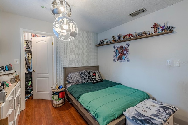 bedroom with visible vents, a textured ceiling, wood finished floors, and wallpapered walls