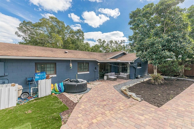 rear view of house with concrete block siding, fence, a shingled roof, outdoor lounge area, and a patio area