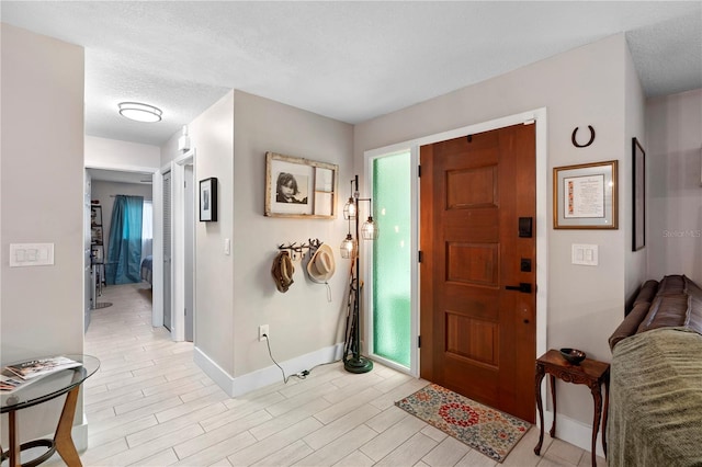 foyer entrance featuring baseboards, a textured ceiling, and light wood finished floors