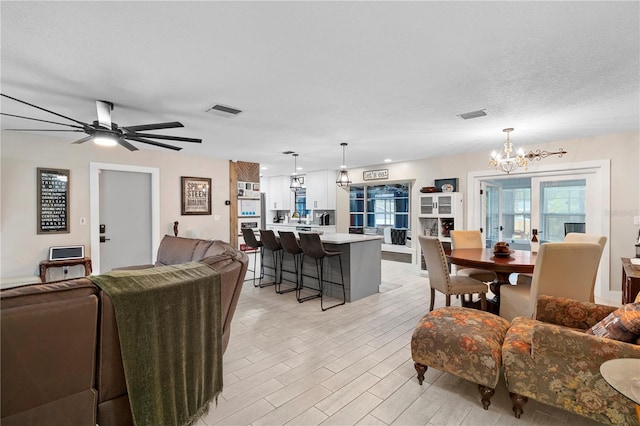 living area featuring ceiling fan with notable chandelier, light wood-style floors, visible vents, and a textured ceiling