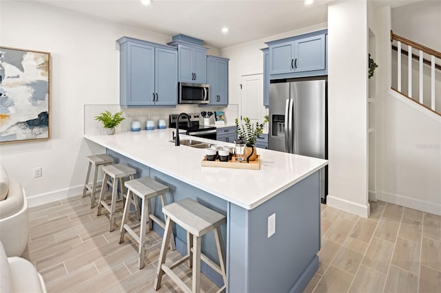 kitchen with blue cabinets, kitchen peninsula, a kitchen bar, decorative backsplash, and appliances with stainless steel finishes