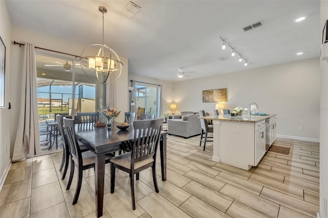 dining area with ceiling fan with notable chandelier, sink, rail lighting, and light hardwood / wood-style flooring