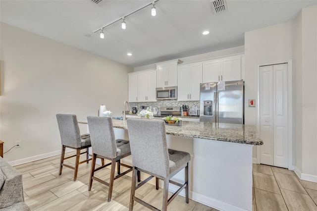 kitchen featuring white cabinets, a kitchen breakfast bar, a kitchen island with sink, and appliances with stainless steel finishes