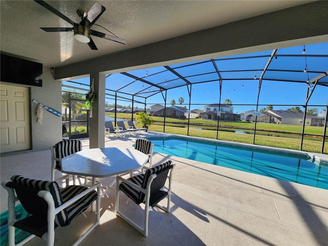 view of swimming pool with glass enclosure, ceiling fan, a patio area, and a lawn