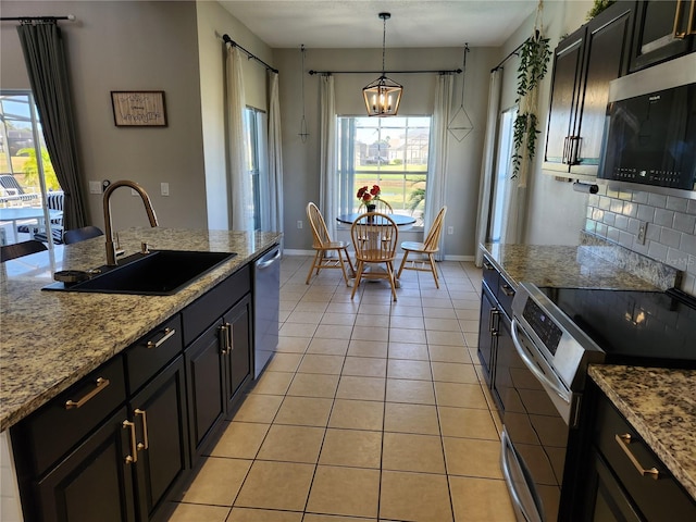 kitchen with appliances with stainless steel finishes, light stone counters, sink, light tile patterned floors, and decorative light fixtures